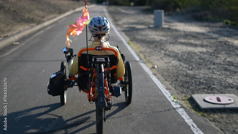 Rear view of elderly senior woman riding a recumbent electric bike on a bike path in Southern California. Filmed in.