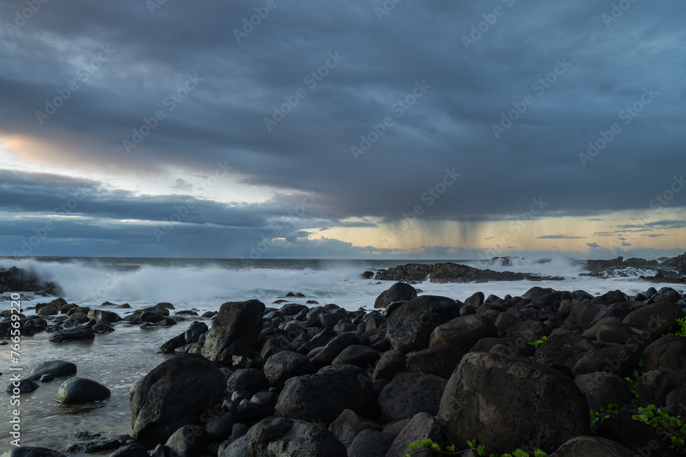 Long exposure shot of the waves crashing on the rocky shore and the rain clouds approaching the coast of Benares beach in a morning on the south coast of Mauritius island
