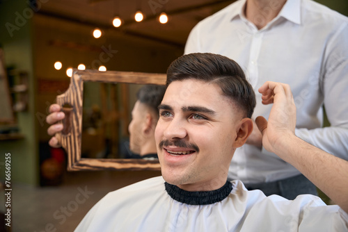 Hairdresser holding mirror and showing result of his work to man