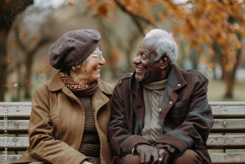 An elderly couple shares a laugh on a park bench, enjoying a warm moment on a crisp autumn day.