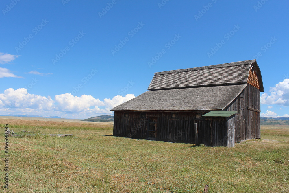 Old farm property in Wyoming. Blue sky and green grass. Clouds in sky. Barn outbuilding in Wyoming countryside with Tetons in the background. Mormon Row outbuildings. Tetons in August. Old farm property in Wyoming. Blue sky and green grass. Clouds in sky. Barn outbuilding in Wyoming countryside with Tetons in the background. Mormon Row outbuildings. Tetons in August.