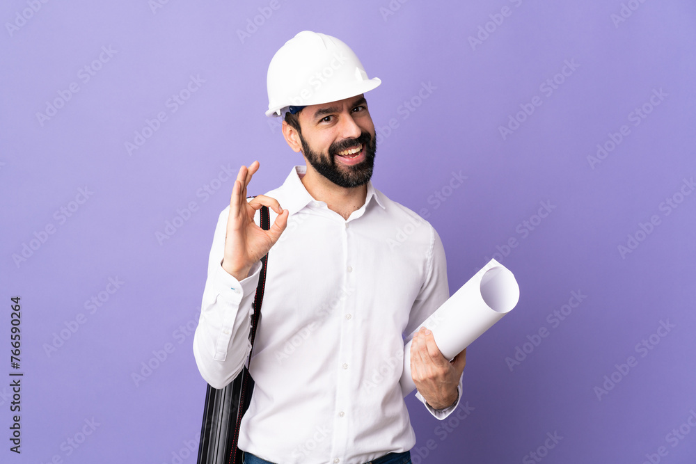 Young architect man with helmet and holding blueprints over isolated purple background showing ok sign with two hands Young architect man with helmet and holding blueprints over isolated purple background showing ok sign with two hands