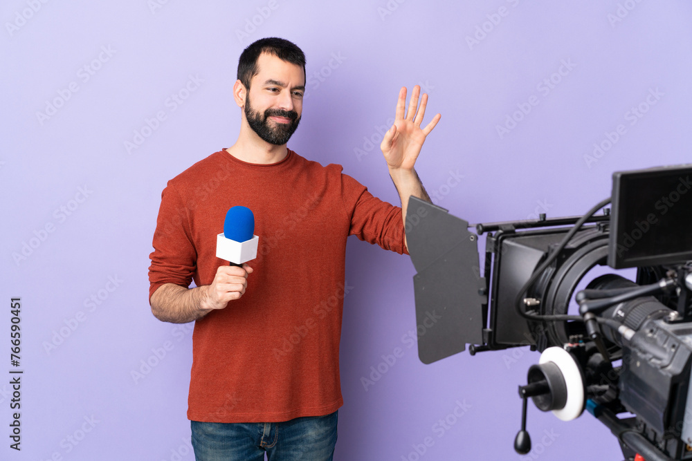 Reporter man holding a microphone and reporting news over isolated purple background saluting with hand with happy expression