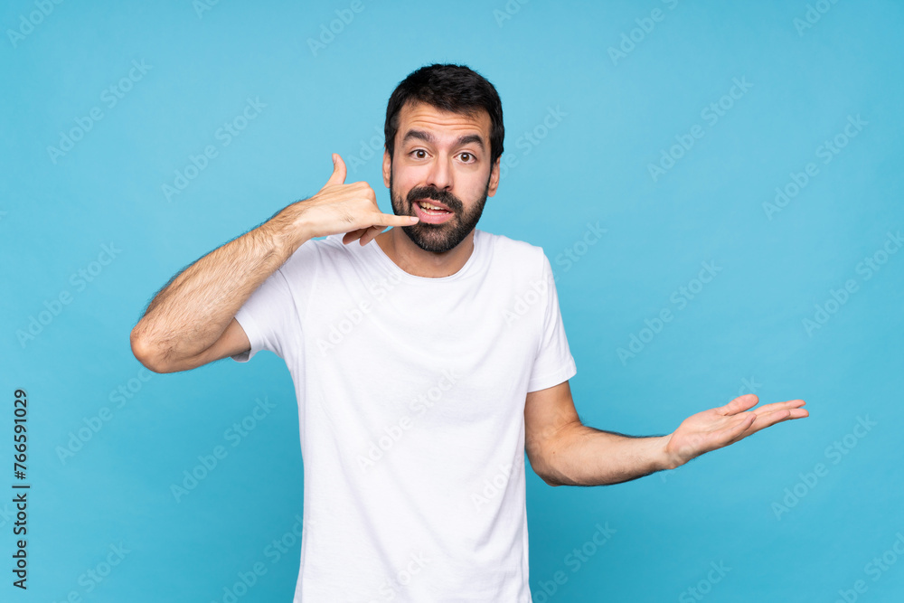 Young man with beard over isolated blue background making phone gesture and doubting Young man with beard over isolated blue background making phone gesture and doubting