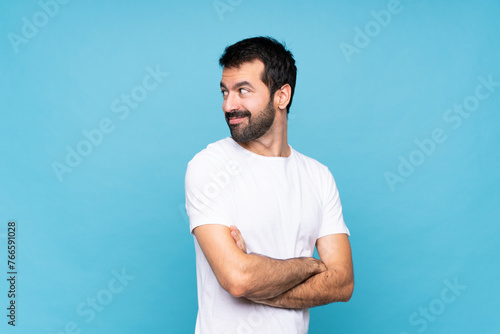 Young man with beard  over isolated blue background with arms crossed and happy © luismolinero