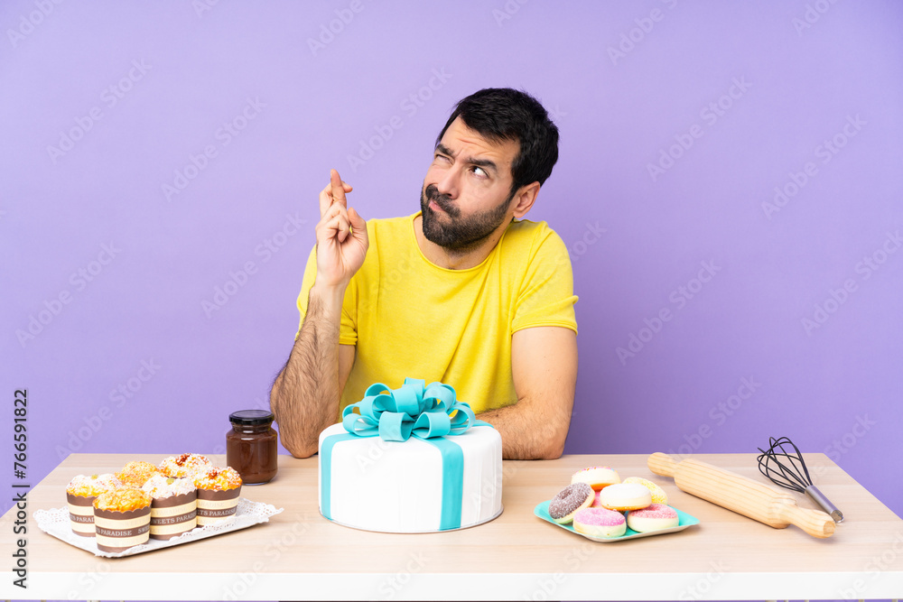 Man in a table with a big cake with fingers crossing and wishing the best Man in a table with a big cake with fingers crossing and wishing the best