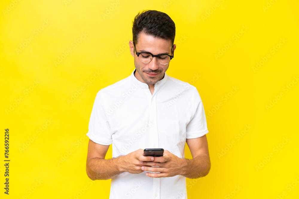 Young handsome man over isolated yellow background sending a message with the mobile Young handsome man over isolated yellow background sending a message with the mobile