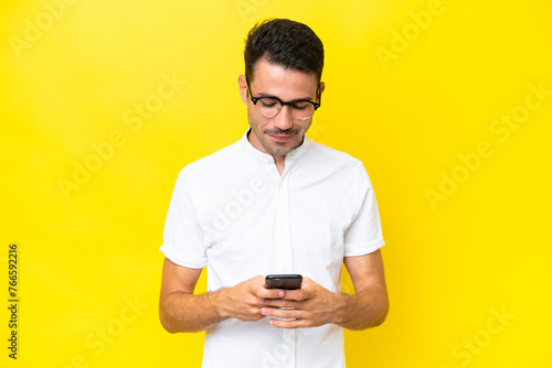 Young handsome man over isolated yellow background sending a message with the mobile © luismolinero