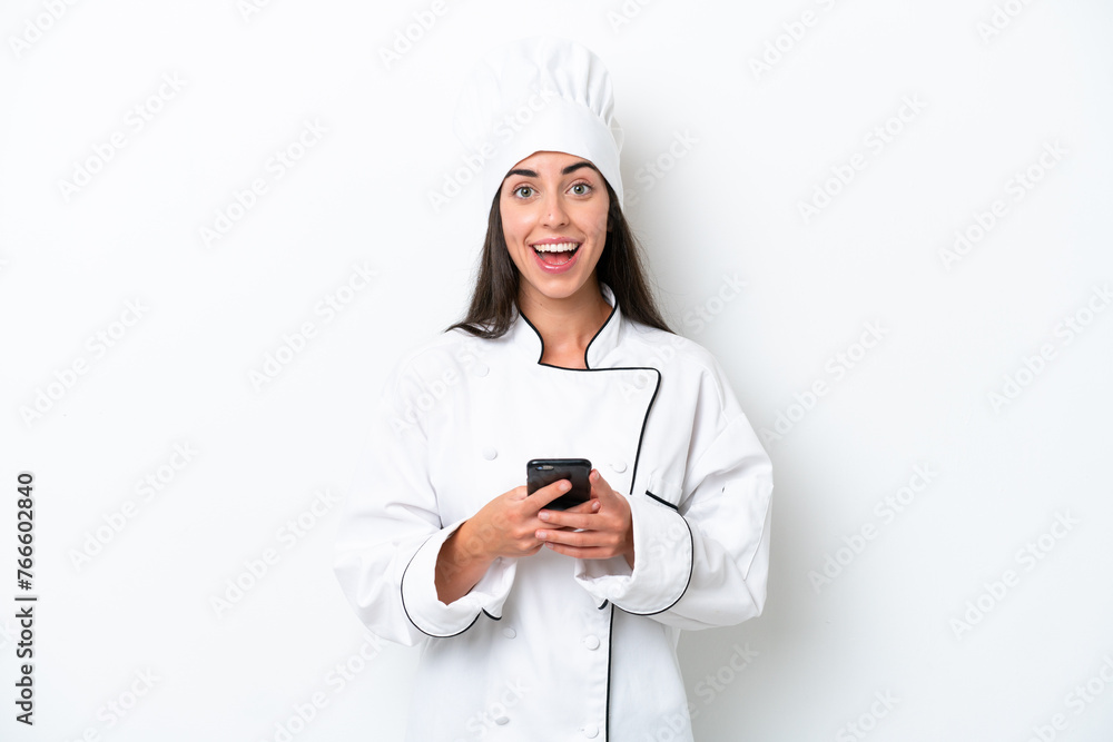 Young chef woman over white background surprised and sending a message Young chef woman over white background surprised and sending a message
