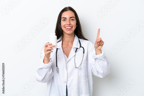 Young caucasian woman isolated on white background wearing a doctor gown and holding pills