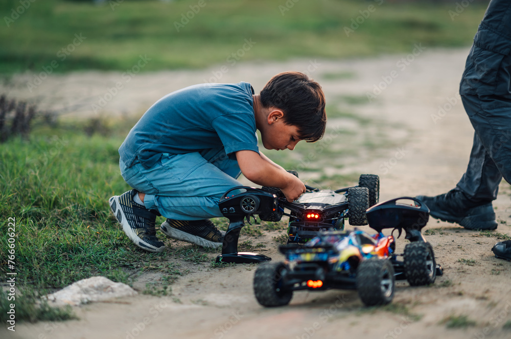 Fototapeta premium Focus frame on a boy examining a turned over toy car on a dirt road.