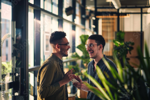 Gen-Z male colleagues laughing and talking in an office, embodying a candid work lifestyle.