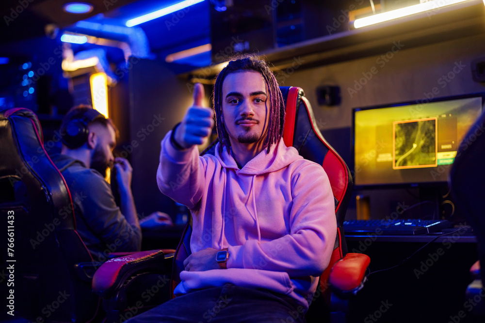 Male gamer with dreadlocks showing thump up and sitting in a gamers chair