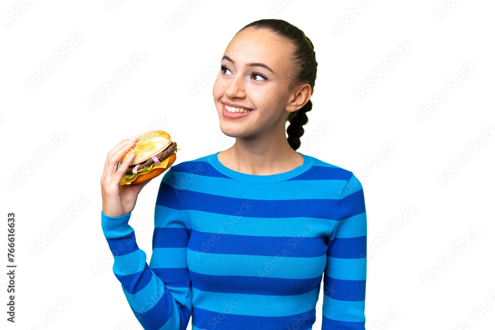 Young Arab woman holding a burger over isolated background thinking an idea while looking up Young Arab woman holding a burger over isolated background thinking an idea while looking up