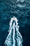 Vue aérienne d'un bateau à moteur blanc se déplaçant dans une eau bleue foncé avec une traînée d'écume blanche 