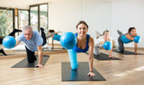 Class of male and women of different ages in active wear working out with mini balls during Pilates training together in rehabilitation center