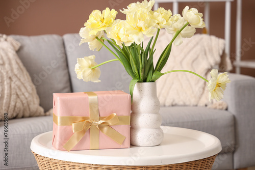Vase with flowers and gift box on coffee table in living room