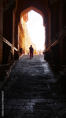 Passage dans une ruelle, allée ou haute porte ouverte, courbée, avec de la pierre et des briques rouges, blanc et orange, quelques personnes, avec escaliers, splendeur architecture d'un fort indien,  photo