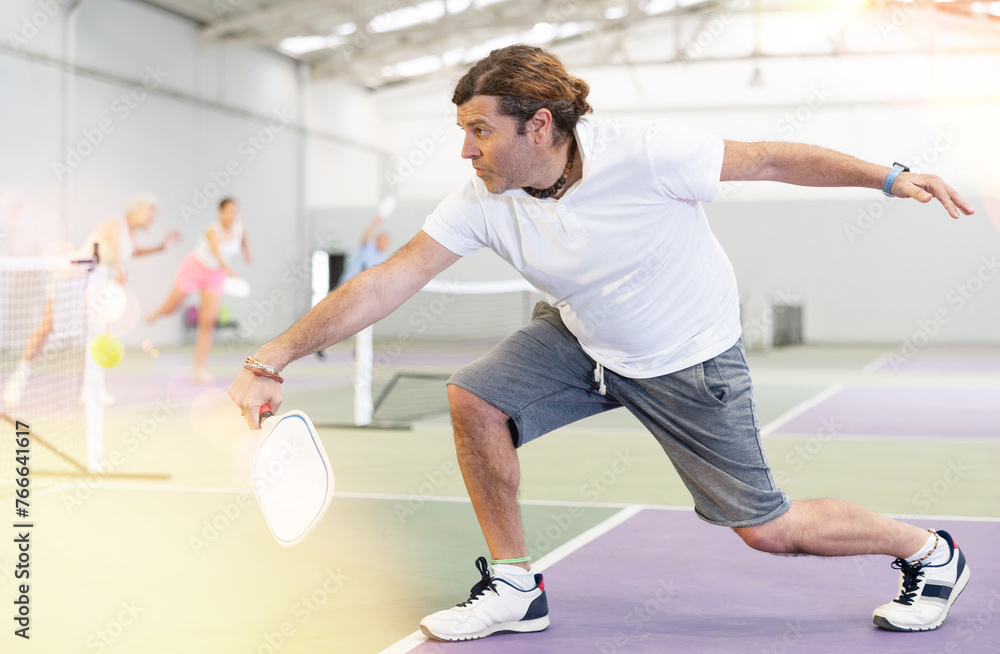 Focused adult man playing friendly pickleball match on small closed court. Concept of concentration in competition.. - obrazy, fototapety, plakaty 