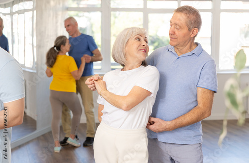 Mature man in dance hall with female partner and dances Latin rumba. Hobby, healthy lifestyle concept