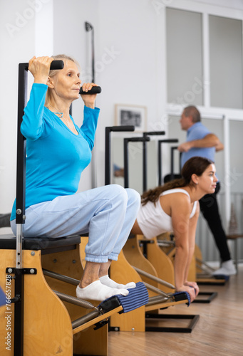 Mature female in activewear concentrating on tone exercise for legs on Pilates chair equipment in gym. Active and healthy lifestyle concept