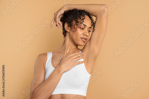 Young latin woman with perfect soft armpit skin enjoying results of routine procedures, ad for under arm deodorant and epilation, beige background