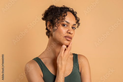 Beautiful young black woman with clean, fresh, glow skin posing and looking at camera on beige background