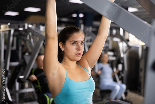 Sporty young woman using shoulder press machine in gym © JackF
