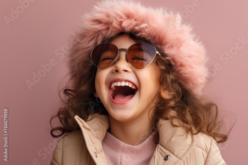 Cute little girl in warm winter coat and sunglasses on pink background