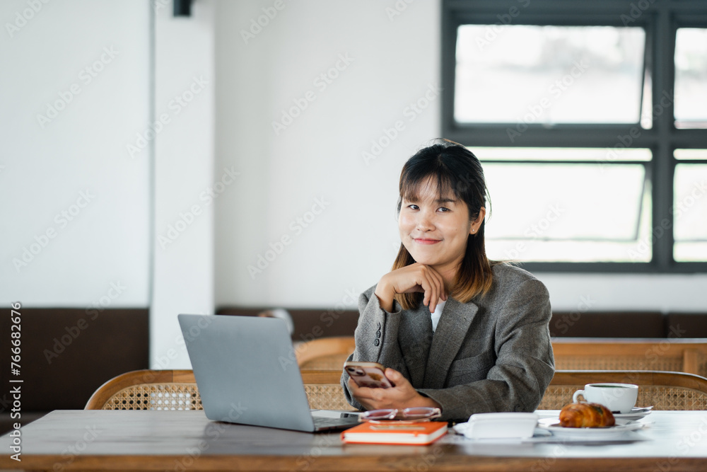 An upbeat businesswoman multitasks with a smartphone and laptop in a cafe, accompanied by coffee and a morning pastry. An upbeat businesswoman multitasks with a smartphone and laptop in a cafe, accompanied by coffee and a morning pastry.
