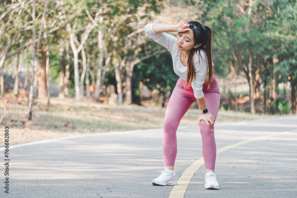 Young woman in sportswear pauses for a rest during a run in a park, wiping sweat from her forehead. Young woman in sportswear pauses for a rest during a run in a park, wiping sweat from her forehead.