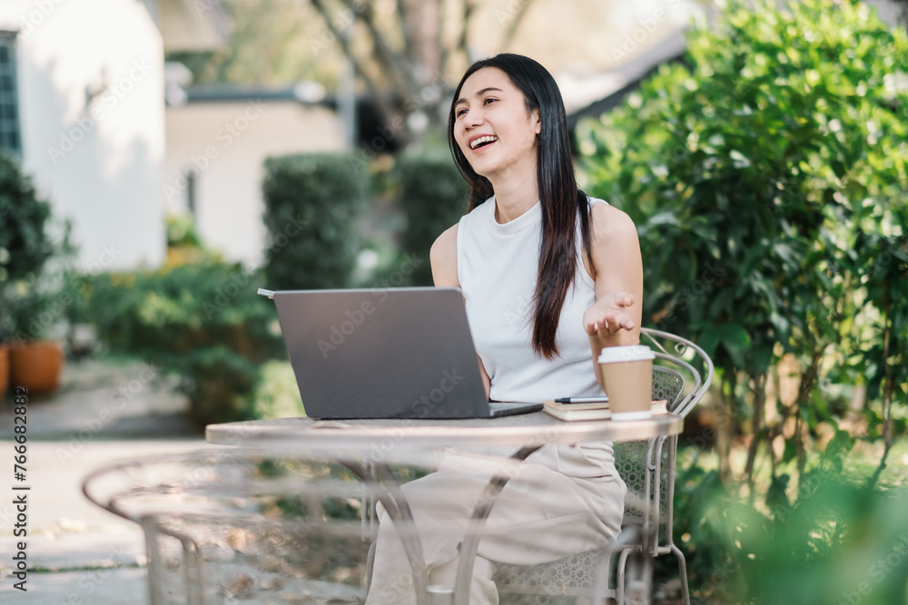 Cheerful woman enjoys working on her laptop at an outdoor table in a lush garden, embodying the freedom of freelancing. Cheerful woman enjoys working on her laptop at an outdoor table in a lush garden, embodying the freedom of freelancing.