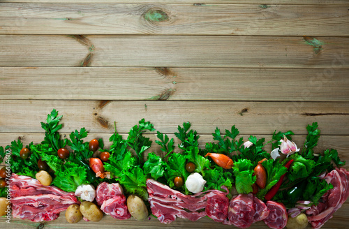 Natural wooden background with raw lamb chops, vegetables, greens and condiments..