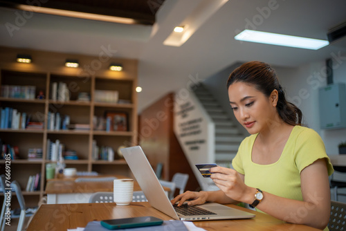 Asian woman sitting and holding credit card for online shopping by laptop and smart phone at home.