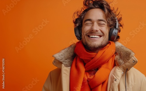 A young man is smiling and holding a cell phone while wearing headphones © hakule