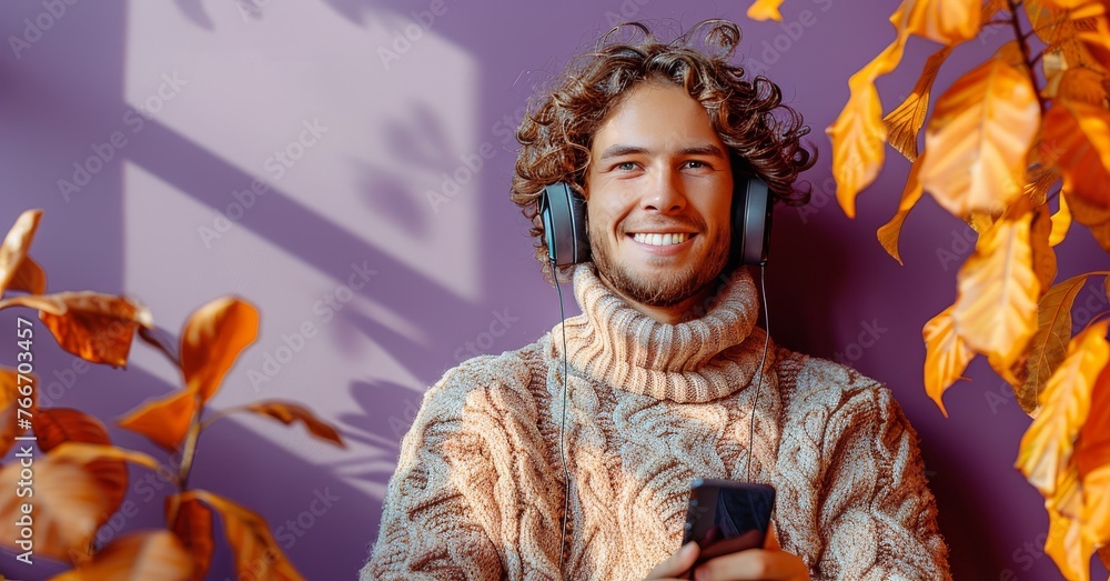 A man wearing a sweater and headphones is smiling and holding a cell phone