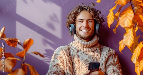 A man wearing a sweater and headphones is smiling and holding a cell phone