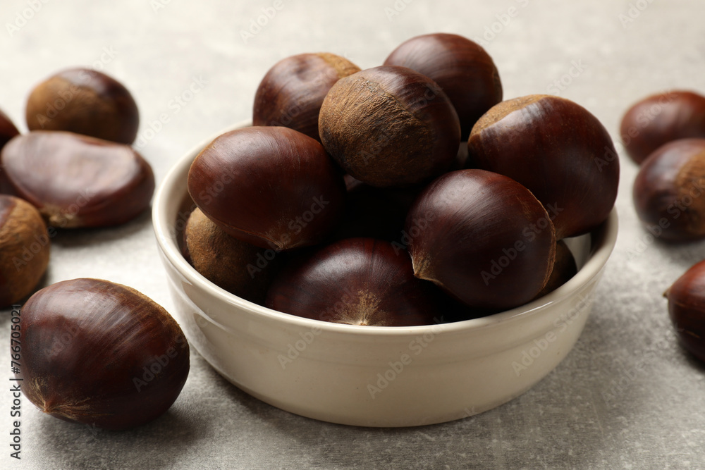 Bowl with roasted edible sweet chestnuts on light grey table, closeup Bowl with roasted edible sweet chestnuts on light grey table, closeup