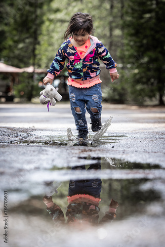 Fototapeta Naklejka Na Ścianę i Meble -  A young girl is playing in the rain, splashing water
