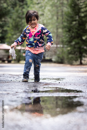 A little girl is playing in the rain, splashing in puddles and holding a toy