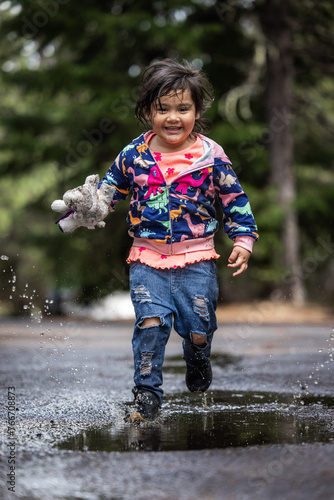 A young girl is playing in the rain, holding a stuffed animal