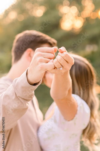 A sunset kiss with an engaged couple with their fingers making a pinkie promise showing off her engagement ring. 