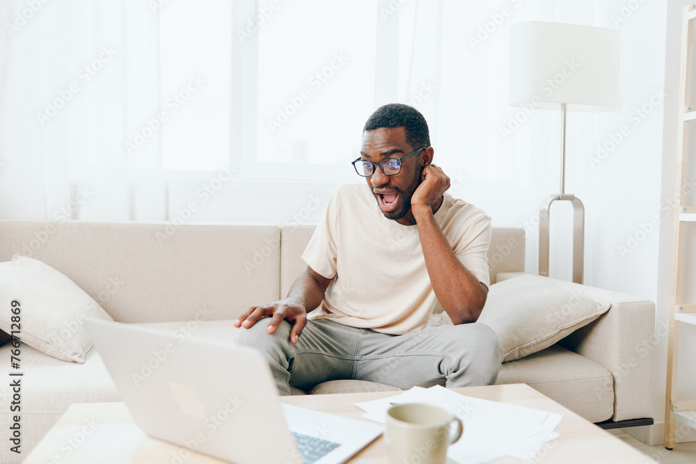 Smiling African American Freelancer Working on Laptop in Modern Home Office or Young African American Man Typing on Laptop in Cozy Living Room Smiling African American Freelancer Working on Laptop in Modern Home Office or Young African American Man Typing on Laptop in Cozy Living Room