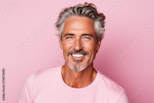 Portrait of a smiling mature man with gray hair and beard standing against pink background
