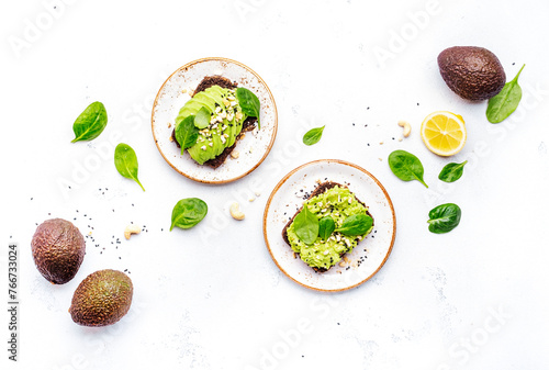 Avocado toasts with spinach and cashew nuts sprinkled with sesame seeds on white table background, top view