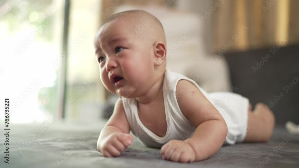A baby is crying on a bed. The baby is wearing a white tank top A baby is crying on a bed. The baby is wearing a white tank top