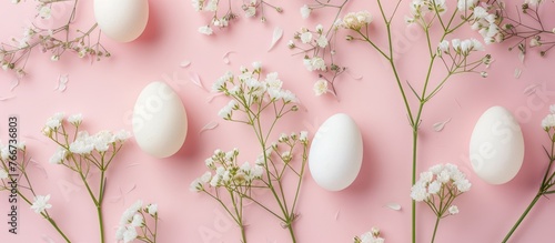 Delicate flowers arranged with chicken eggs on a pink background for Easter, captured from above.