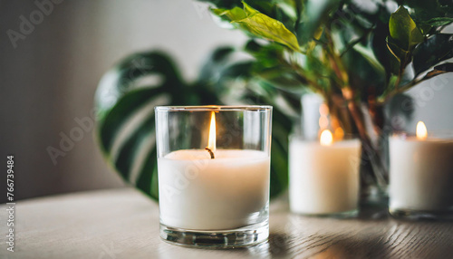 Burning white candles in glass amidst plants, evoking calmness 