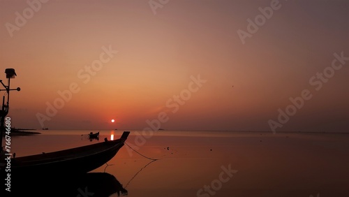 In the tranquil ambiance of Ko Pha Ngan, Thailand, the island's silhouette dances against the twilight sky, casting mesmerizing shadows over the sea as the sun sets in a breathtaking display of orange