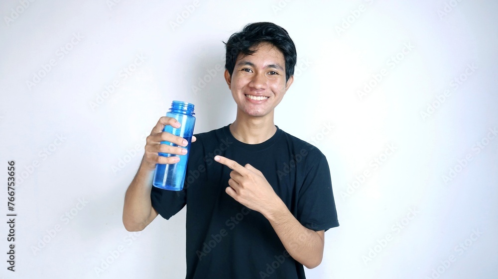 Handsome young Asian man smiling gesturing holding and pointing at a drinking water bottle Handsome young Asian man smiling gesturing holding and pointing at a drinking water bottle